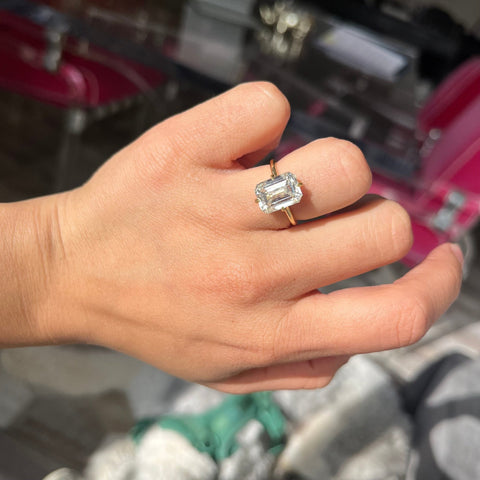 5.01ct Emerald Cut Diamond solitaire ring in yellow gold with hidden halo shown on ring finger
