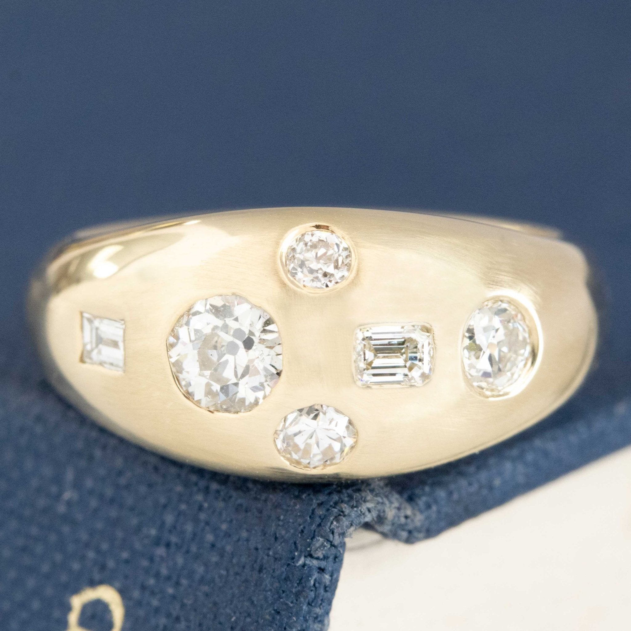 .57ctw Mixed Cut Diamond Bombe Ring with mixed cut diamonds set in a random pattern, resting on a blue textured surface. Antique-inspired one-of-a-kind wedding band.