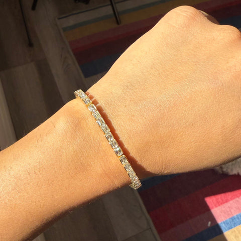 Full view of modern diamond tennis bracelet on model. Gold bezel-set diamond tennis bracelet sparkling under natural light