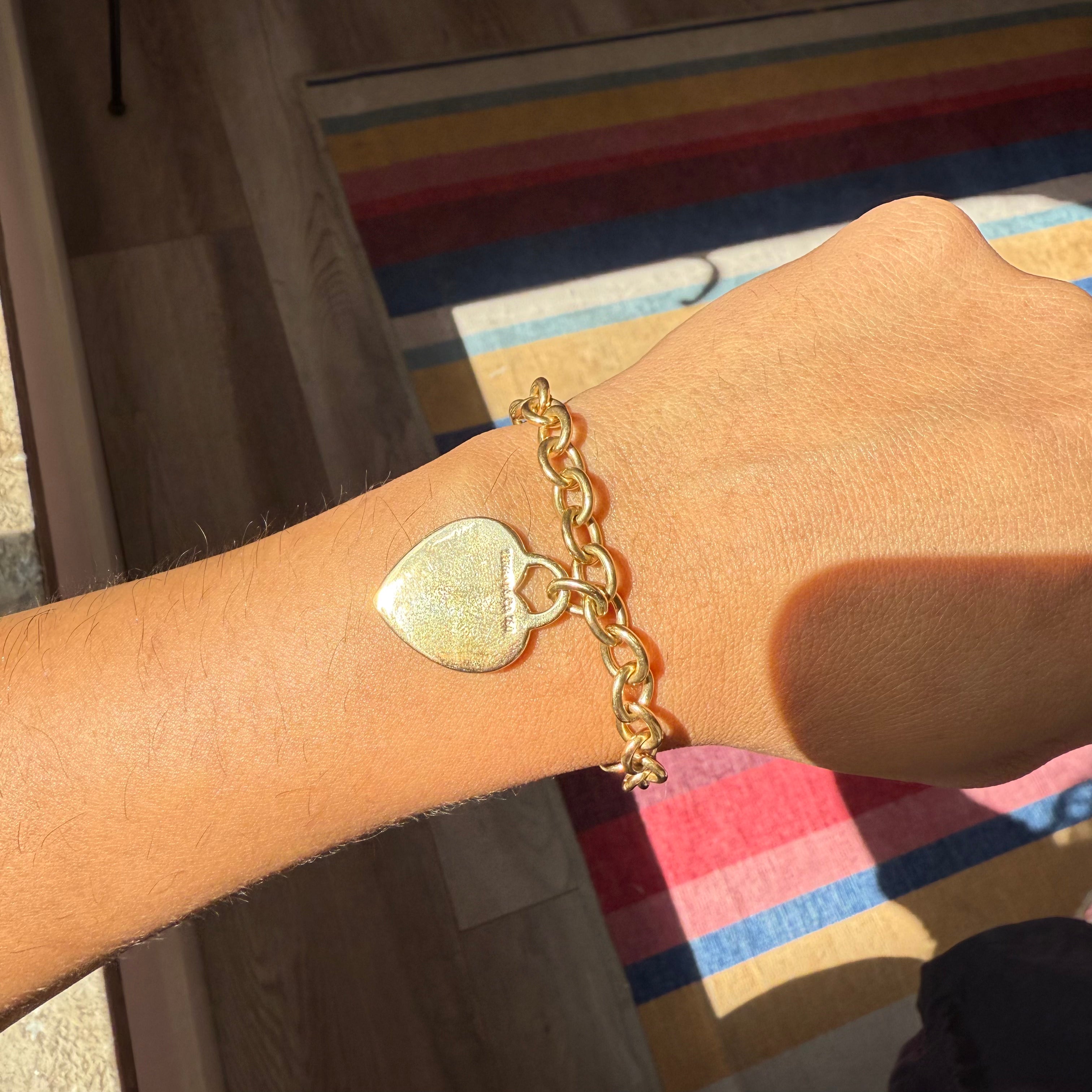 Solid 18kt gold cable link bracelet by Tiffany with classic heart tag. Shown on a wrist