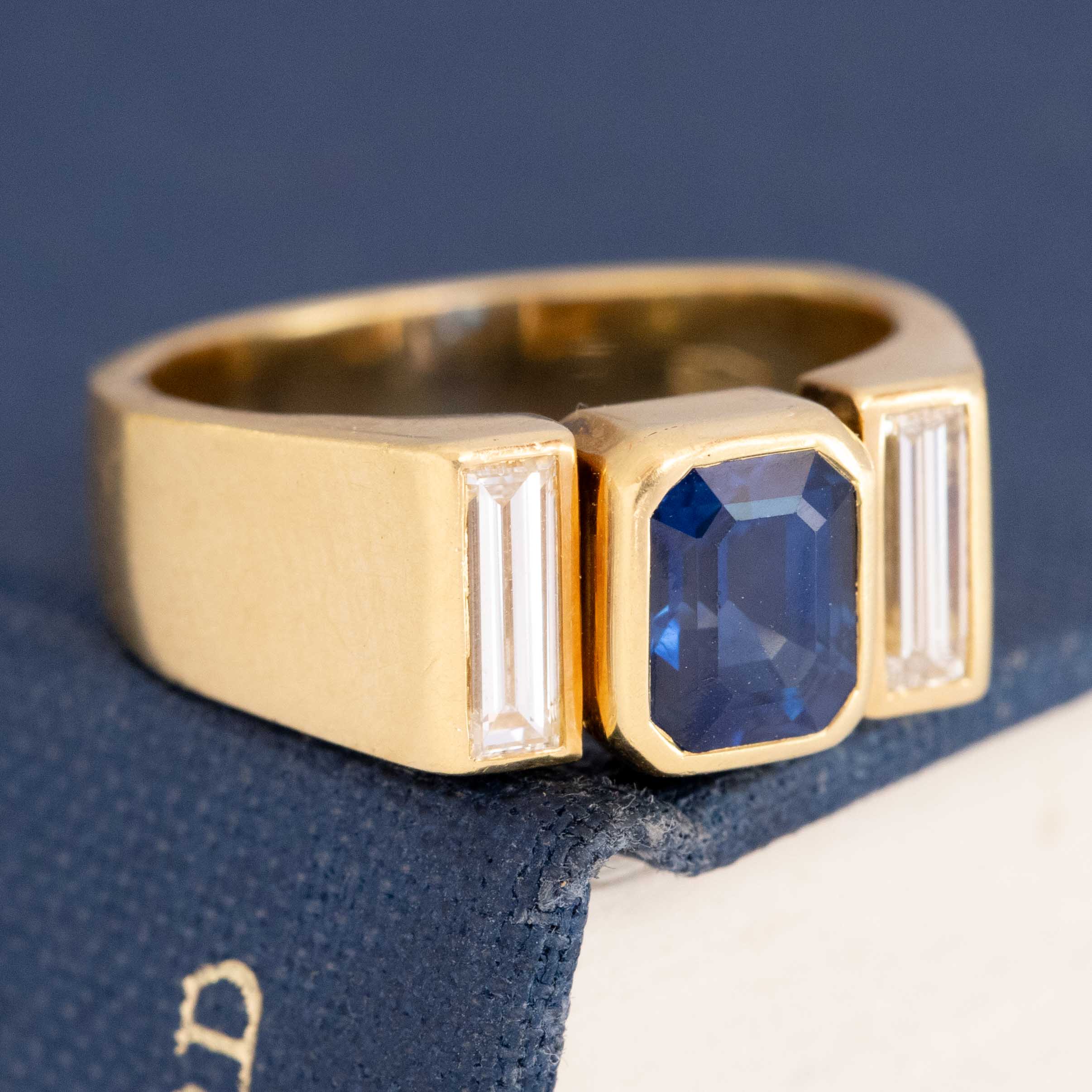 Close-up of deep blue emerald-cut sapphire and vertical baguette diamonds in bezel/tension setting