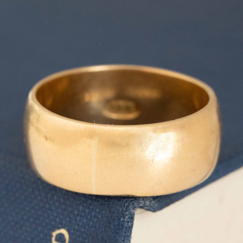 A gold-colored, antique wide band ring laying on a blue textured surface.