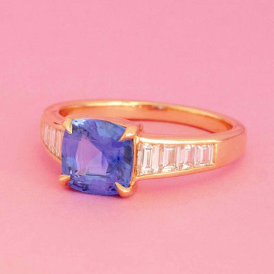 Cushion cut blue sapphire ring with tapered baguette diamonds in 18kt yellow gold on pink background
