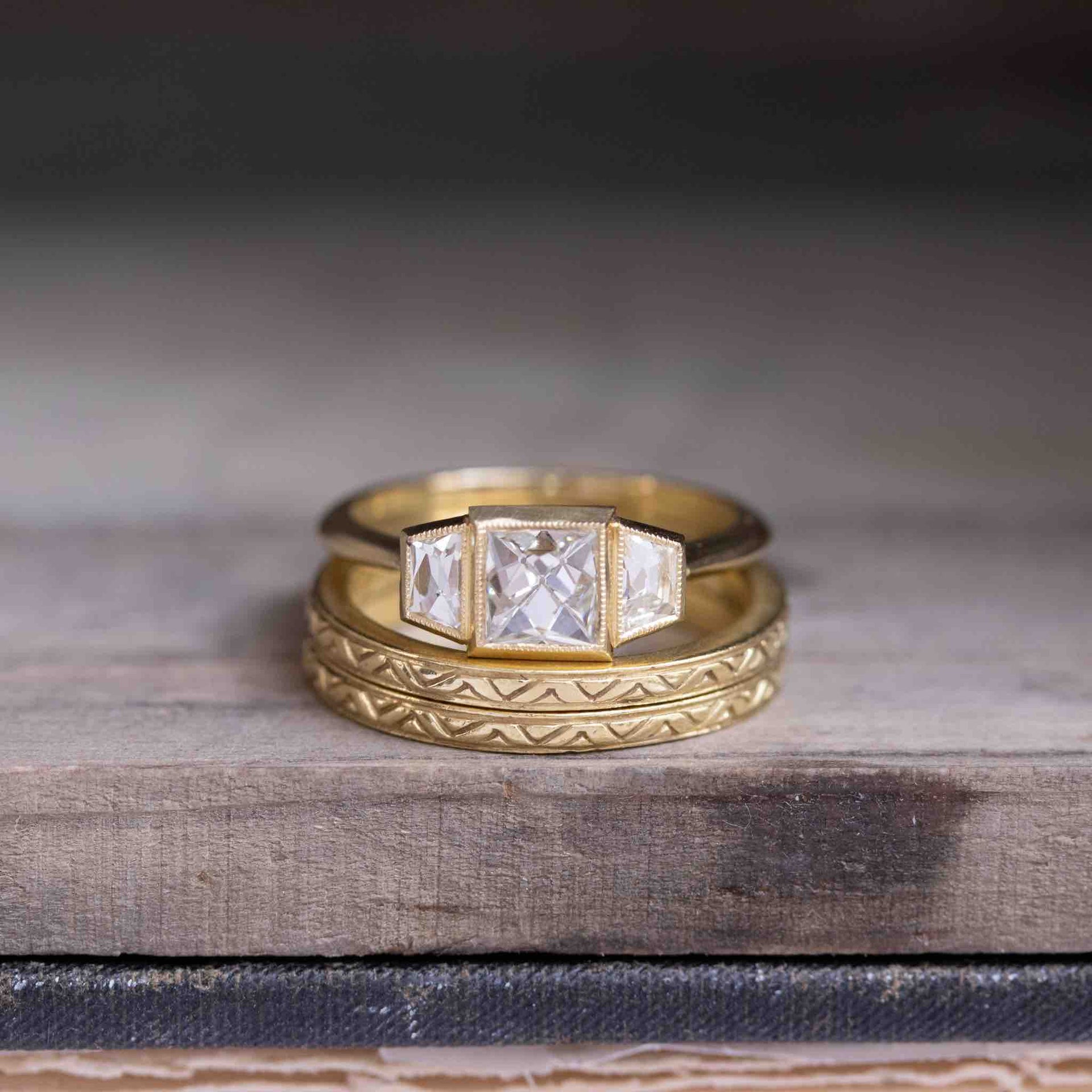 French cut bezel-set diamond trilogy ring paired with two vintage gold bands featuring intricate engraving and etched detailing