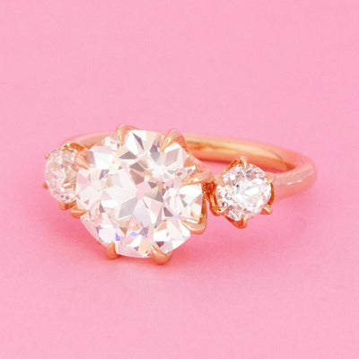 3-stone old European cut diamond trilogy ring in 14kt yellow gold with GIA center stone on pink background