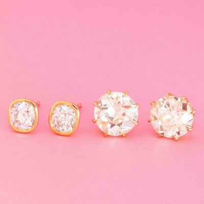 Two pairs of antique diamond stud earrings—old mine cut in bezel yellow gold and old European cut in prong settings on pink background