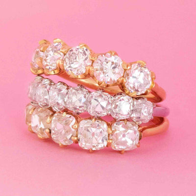 Stack of three half-eternity bands with antique cut diamonds in yellow gold and platinum settings on pink background