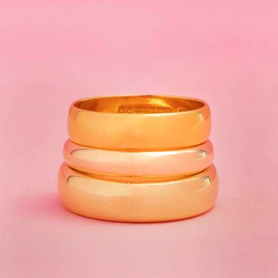Stack of three vintage gold wedding bands in warm yellow gold on pink background