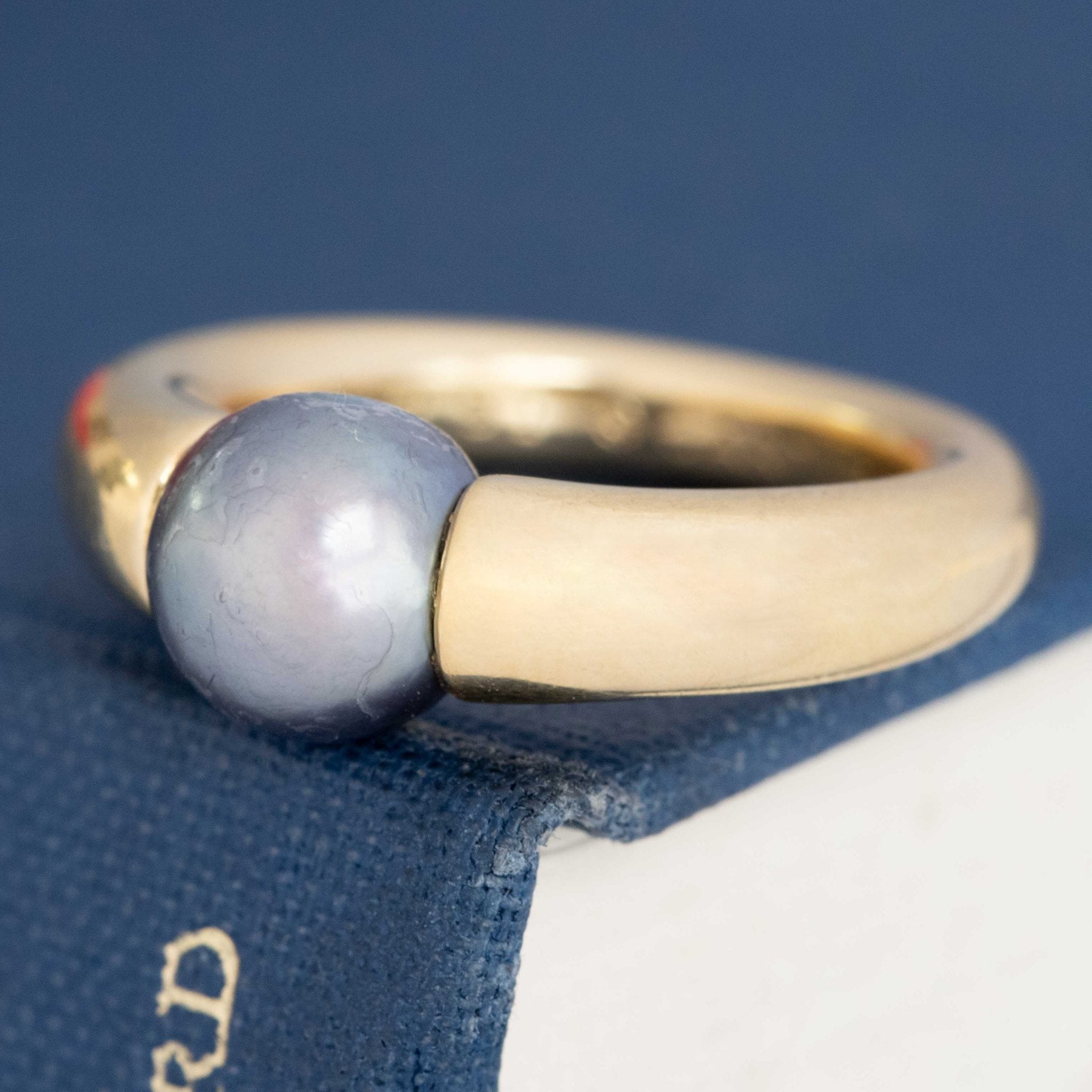 Signed Cartier 90s ring with black pearl in tension setting, crafted in buttery 18k yellow gold.