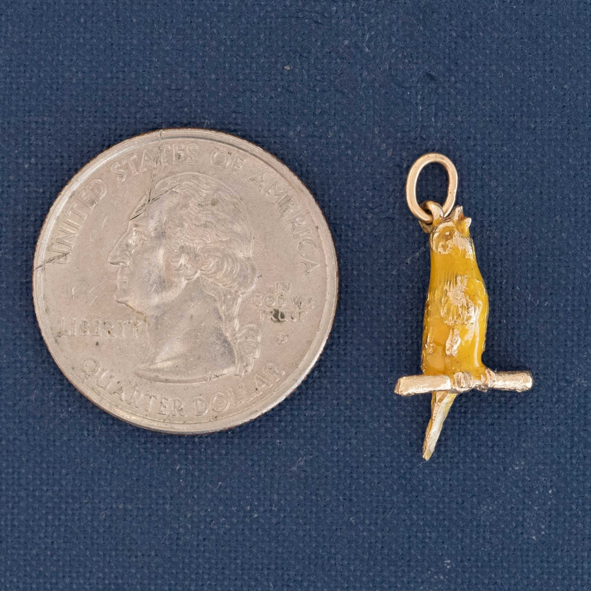 14k gold vintage charm depicting a canary on branch, enamel detailing visible shown next to a quarter for size reference