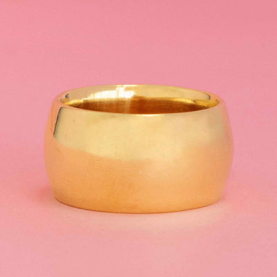 Wide vintage gold cigar band ring with smooth finish on pink background