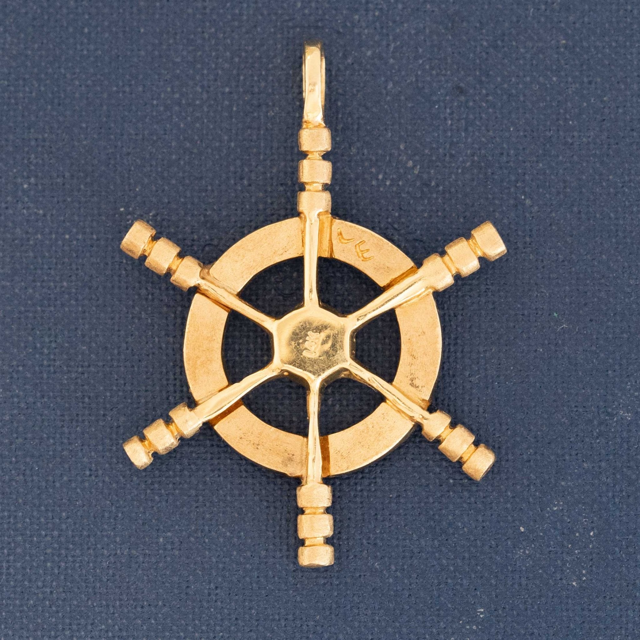 Close-up of yellow gold ship wheel pendant with six spokes, vintage nautical design.