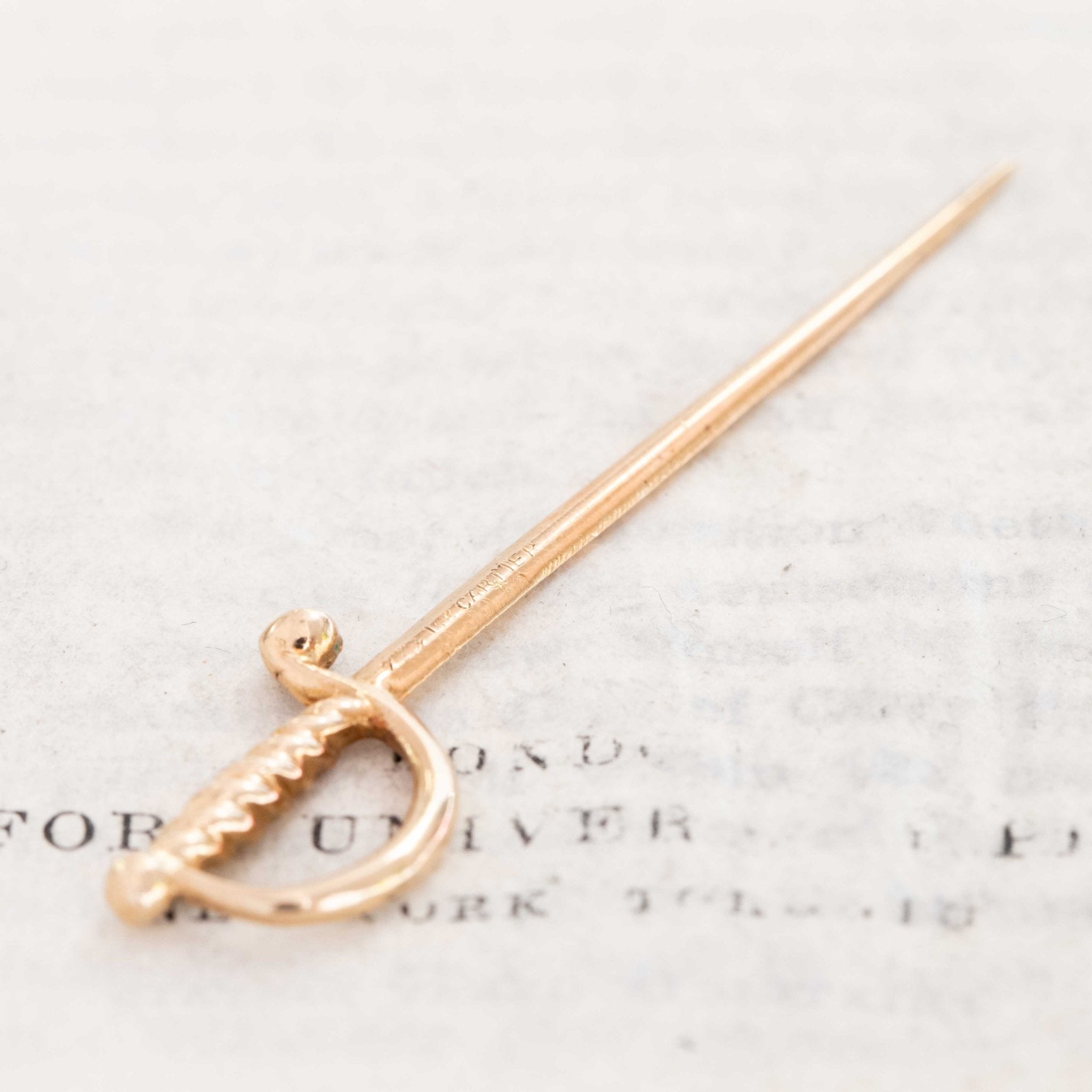 Elegant vintage Cartier sword pin in yellow gold, fine jewelry collectible from the 1950s–1960s.
Flat lay of Cartier vintage gold sword charm, finely crafted 18k collectible accessory.