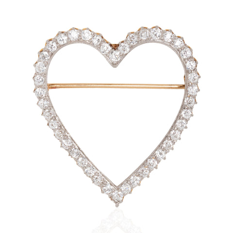 A heart-shaped open brooch featuring a border of clear round-cut stones in a silver-toned setting with a thin gold-toned horizontal pin bar across the center, shown on a white background.
