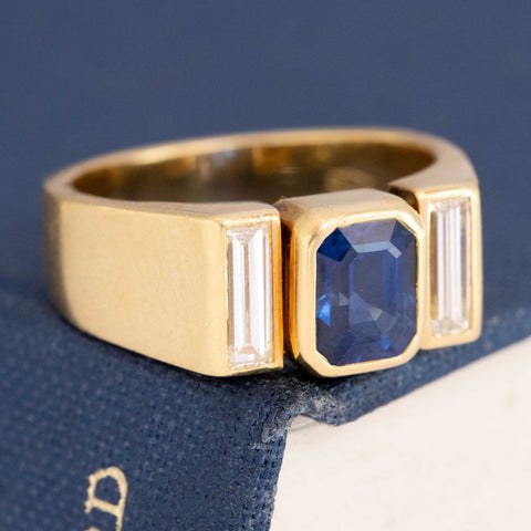 Close-up of deep blue emerald-cut sapphire and vertical baguette diamonds in bezel/tension setting