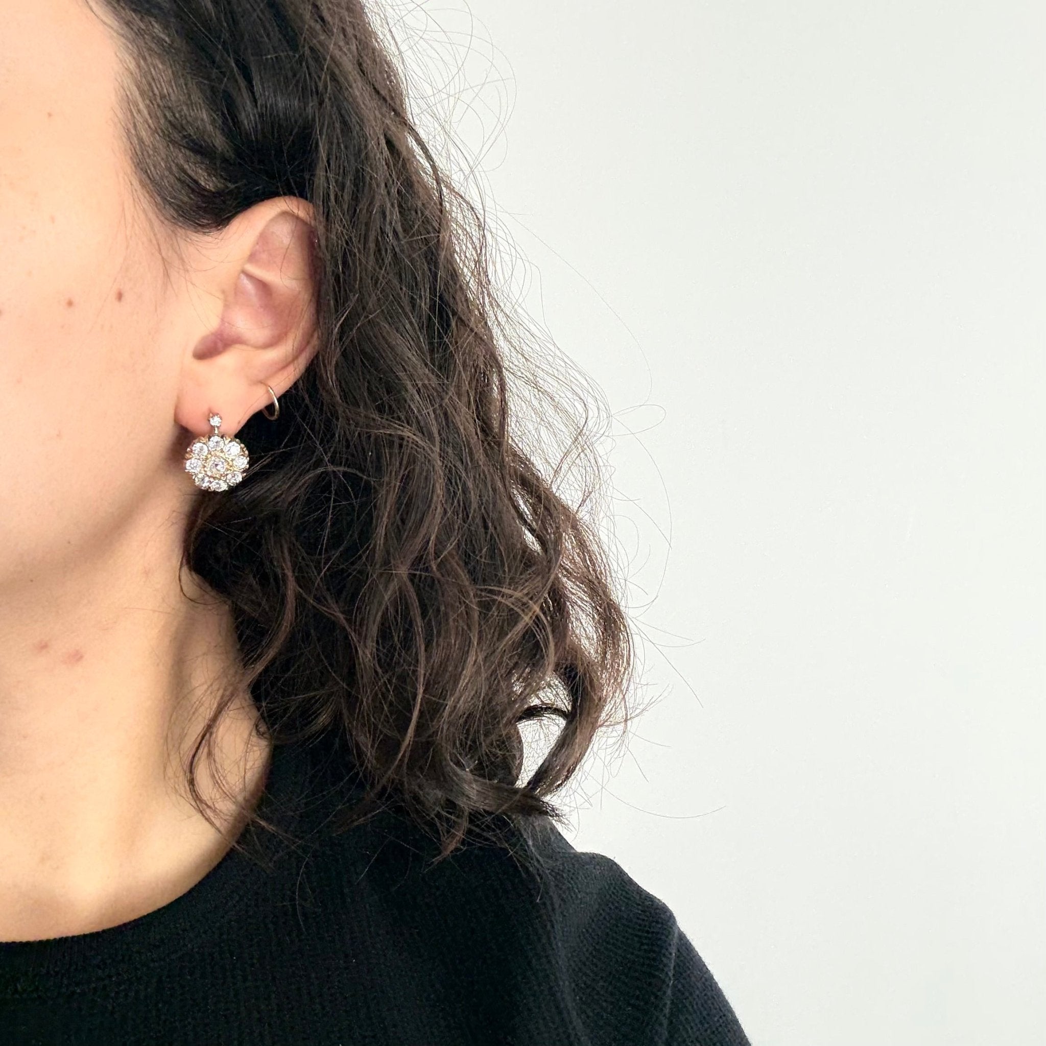 Close-up of a person wearing a diamond earring against a plain background