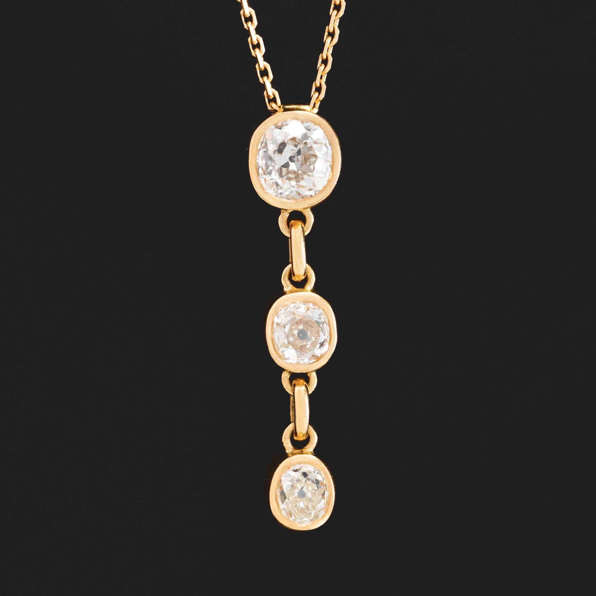 Gold necklace with three diamond pendants on a black background