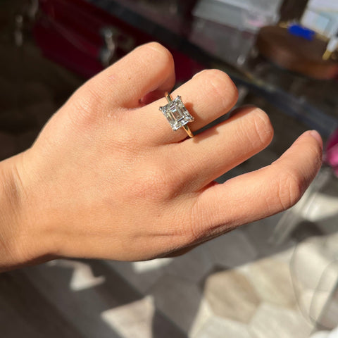 Sleek four-prong emerald cut diamond solitaire with modern vintage design shown on ring finger.