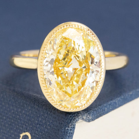 4.70ct Fancy Yellow Oval Diamond bezel solitaire ring in yellow gold.