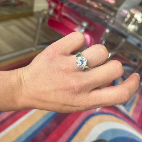 Victorian-inspired three-stone ring with old mine cut diamond and kite-shaped emeralds shown on model.