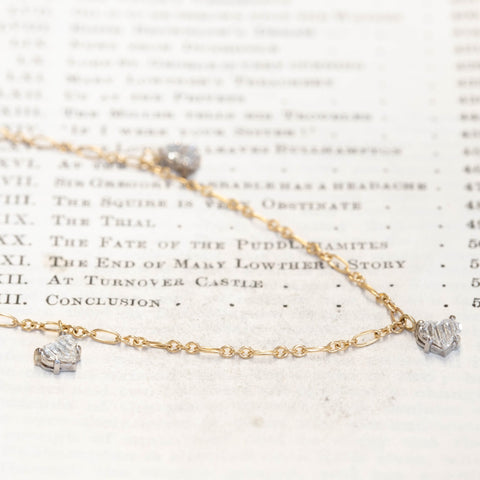 A delicate gold diamond station necklace with heart step cut diamonds displayed on a vintage book page.