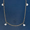 A delicate gold chain necklace featuring four dangling heart step cut diamonds spaced evenly along the chain, displayed against a textured dark blue background.