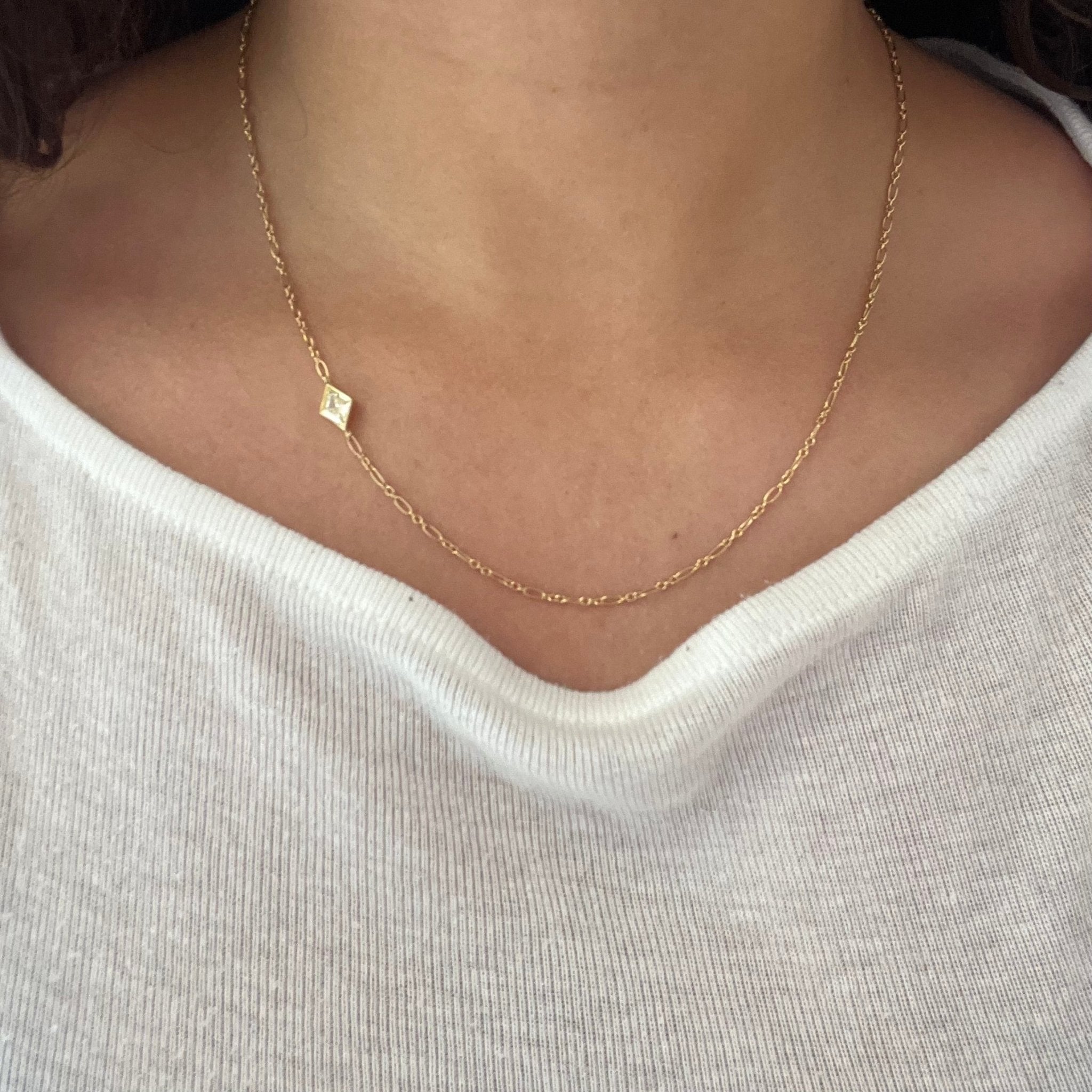 Unique solitaire necklace with .90ct kite diamond placed on the side of a gold chain. Being worn on a neck.
