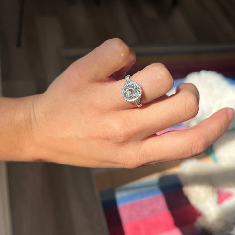 Antique-inspired bezel diamond ring ring with floral motifs and milgrain shown on ring finger