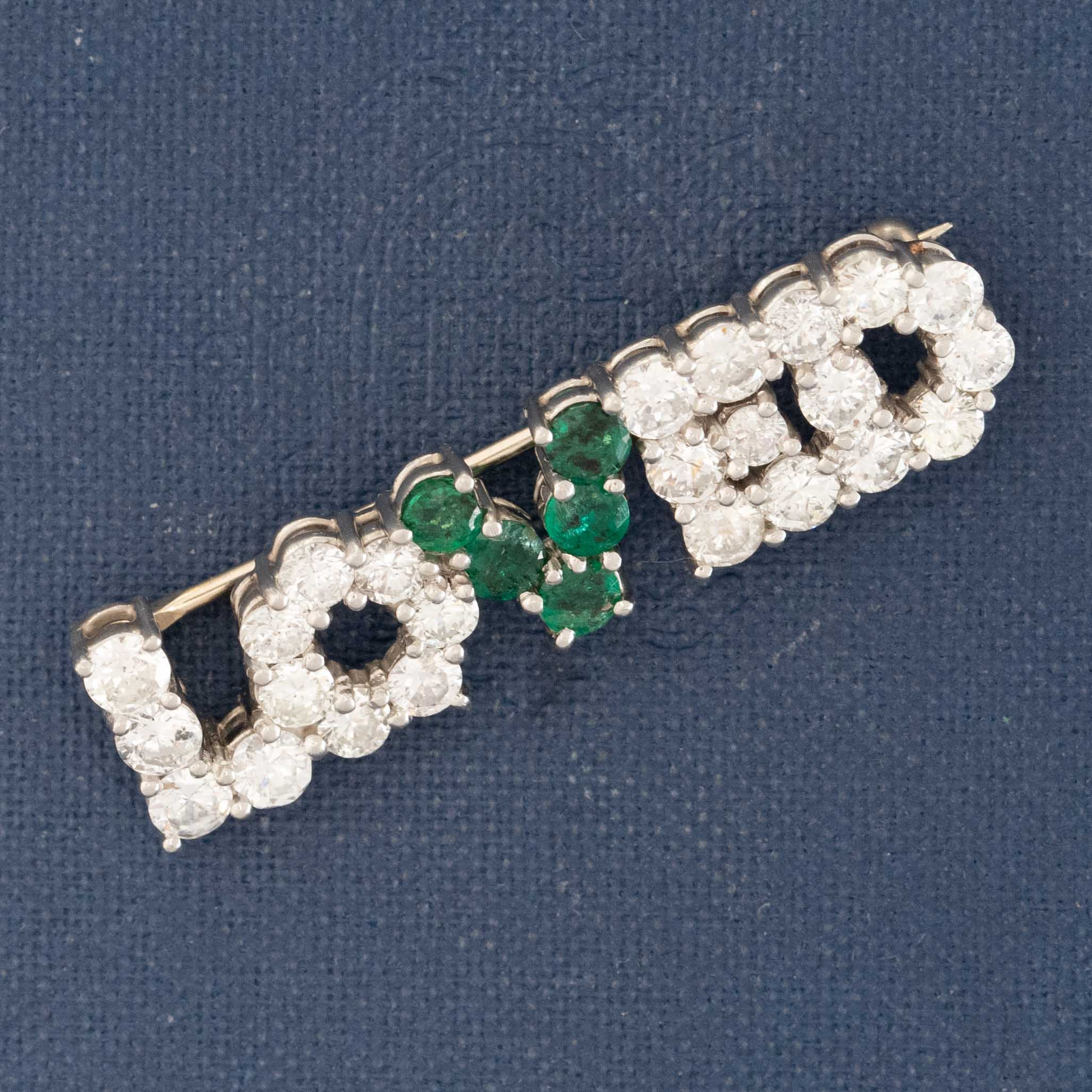 Jewelry piece with 'LOVE' letters featuring emeralds and diamonds on a blue background
