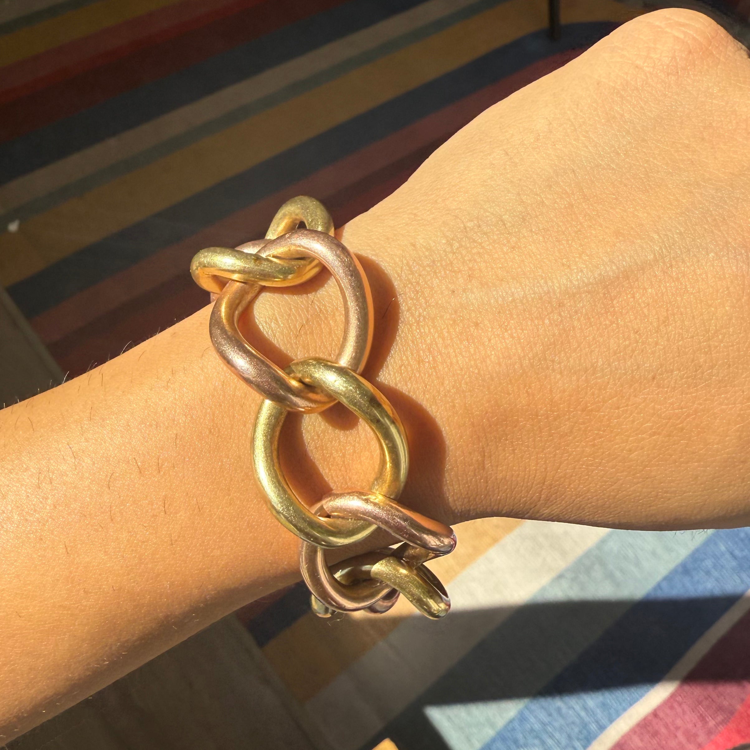 Gold chain bracelet on a wrist with a striped background