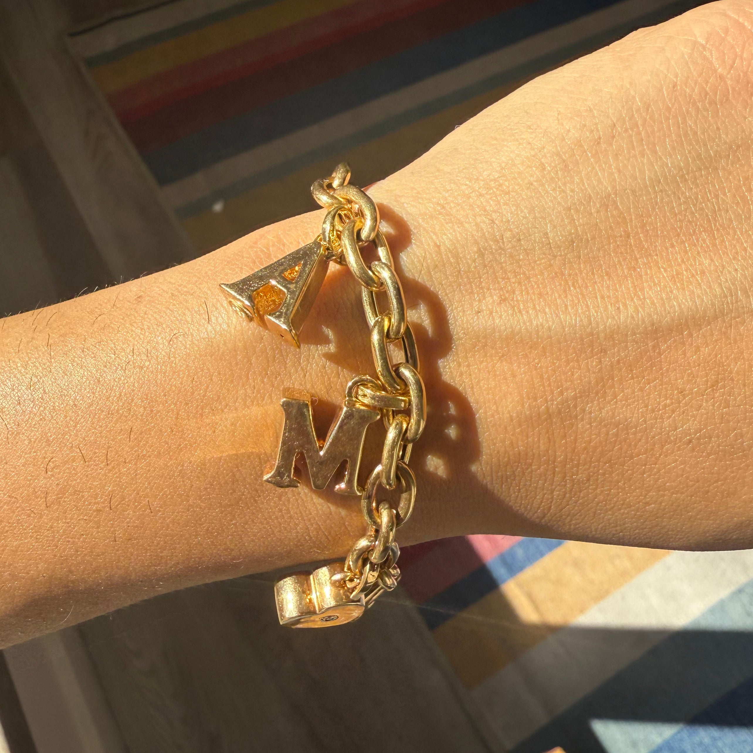 Gold chain bracelet with charms on a wrist against a blurred background