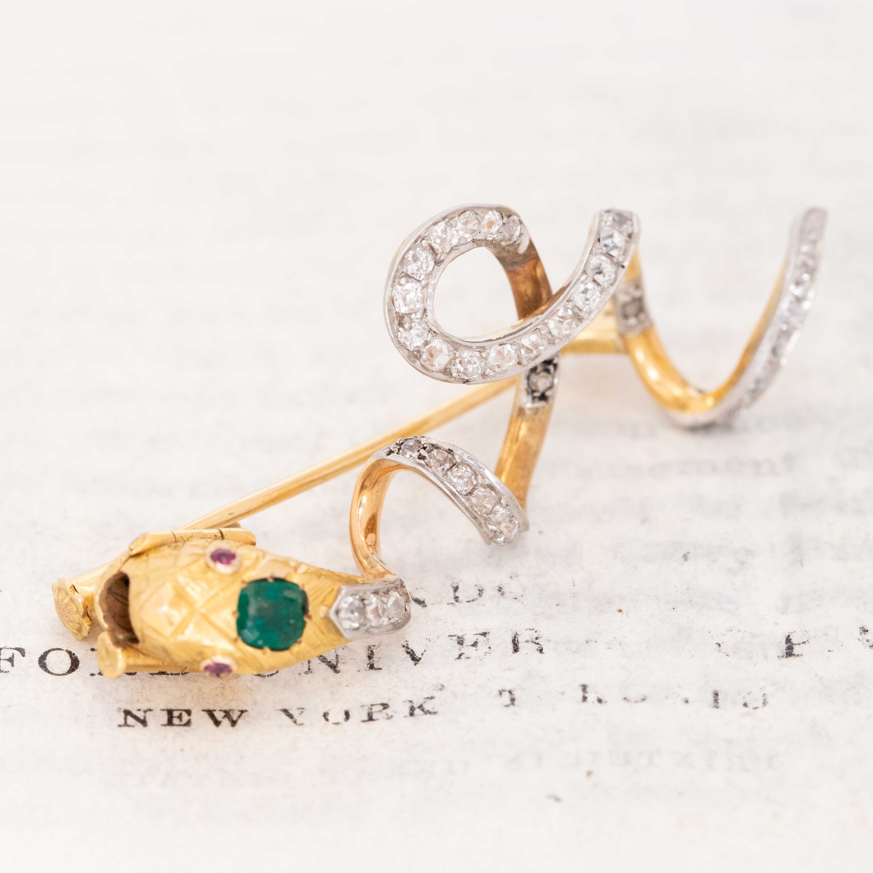 Victorian diamond serpent slider brooch with emerald and ruby accents on antique paper