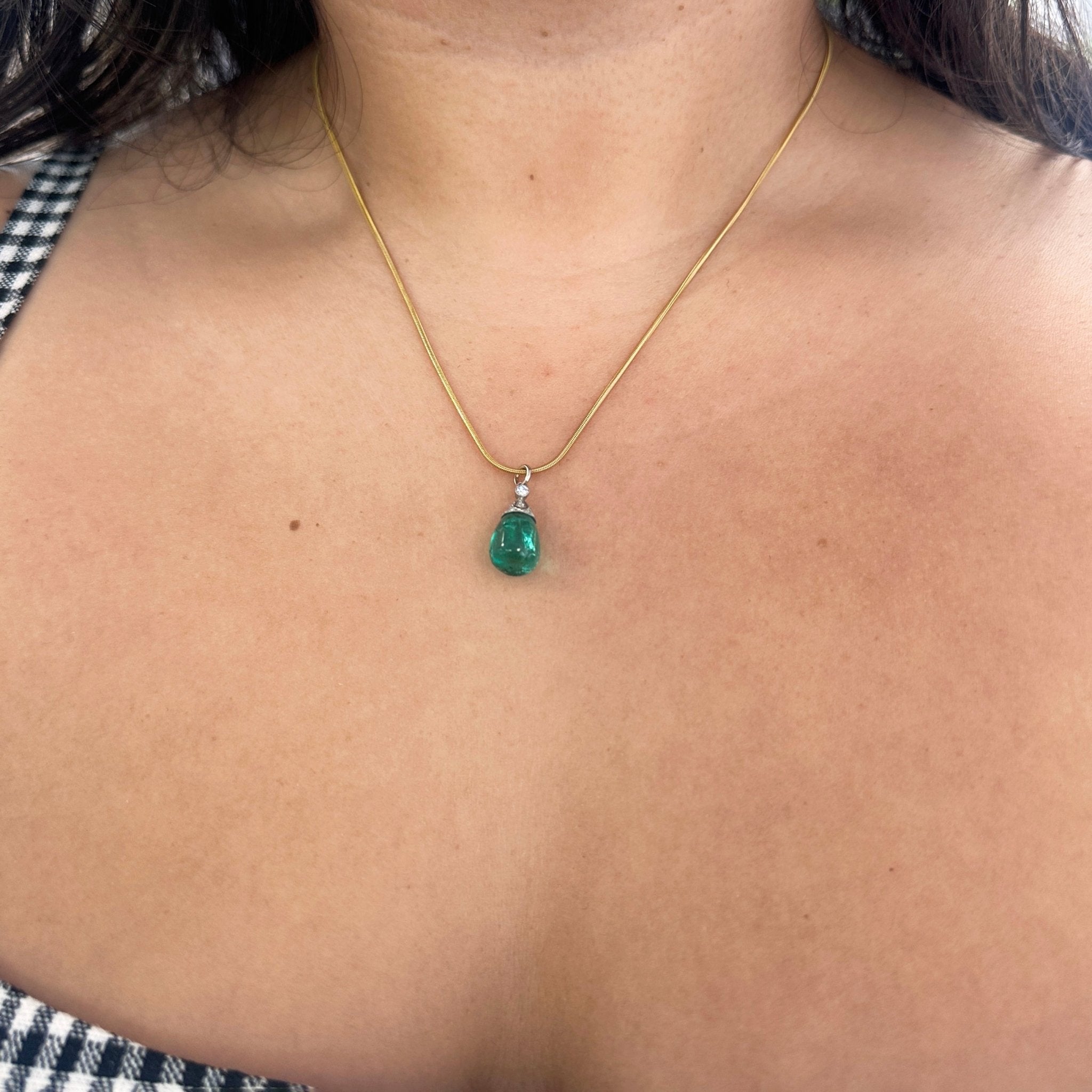 An antique Colombian emerald bead pendant with a beautiful, rich, and desirable color.  Strung on an antique component with diamonds.  Shown against the skin.