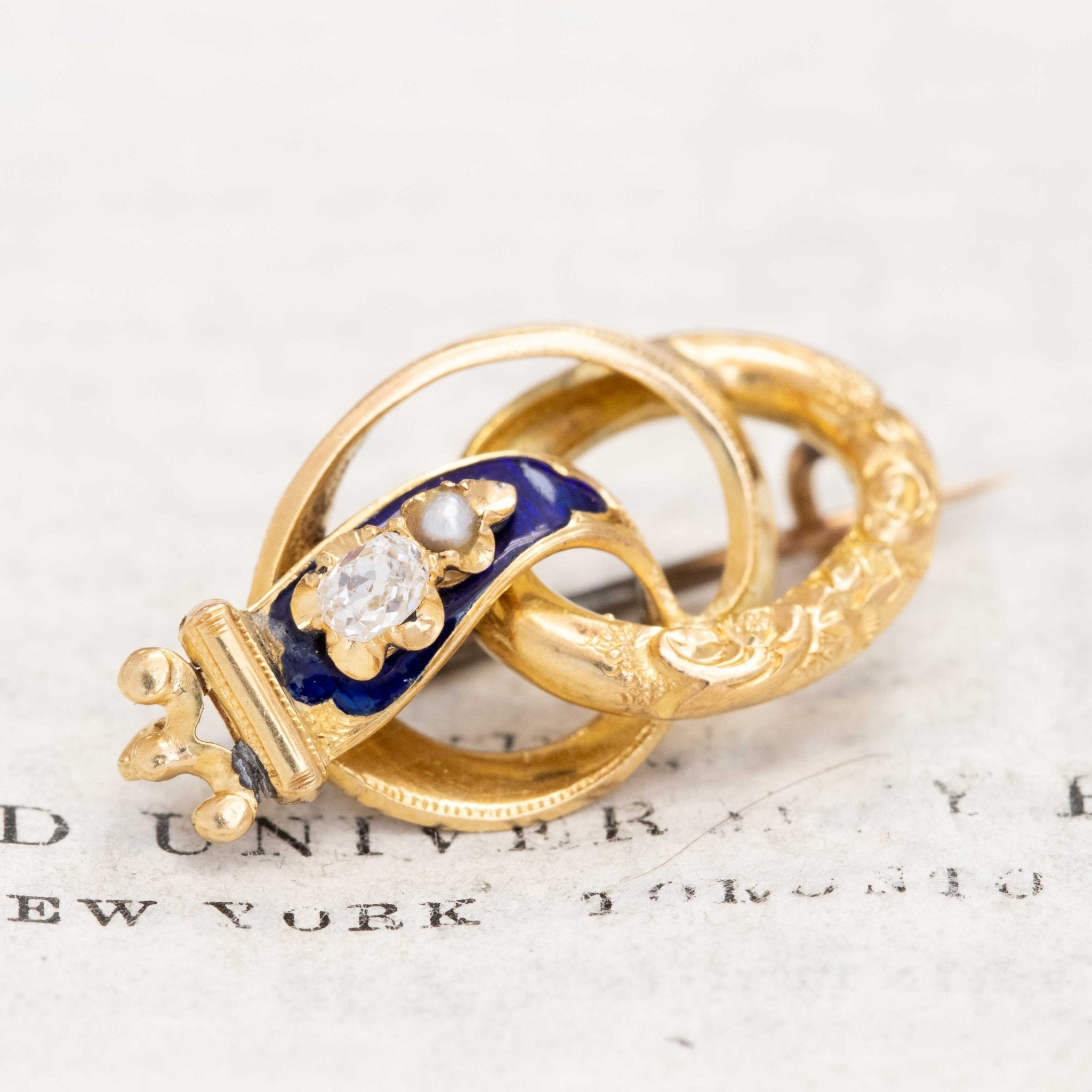 Victorian antique crowned serpent brooch in engraved gold with deep blue enamel, set with a diamond and seed pearl, symbolizing eternal love and triumph.