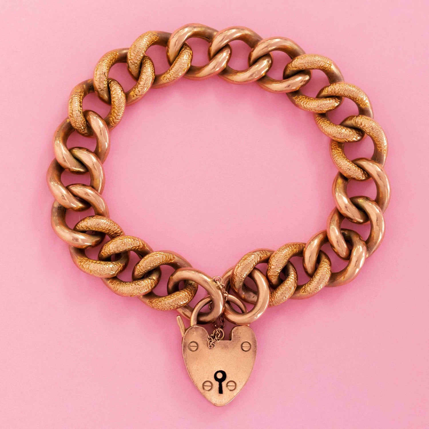 Victorian gold chain bracelet with heart padlock clasp on pink background