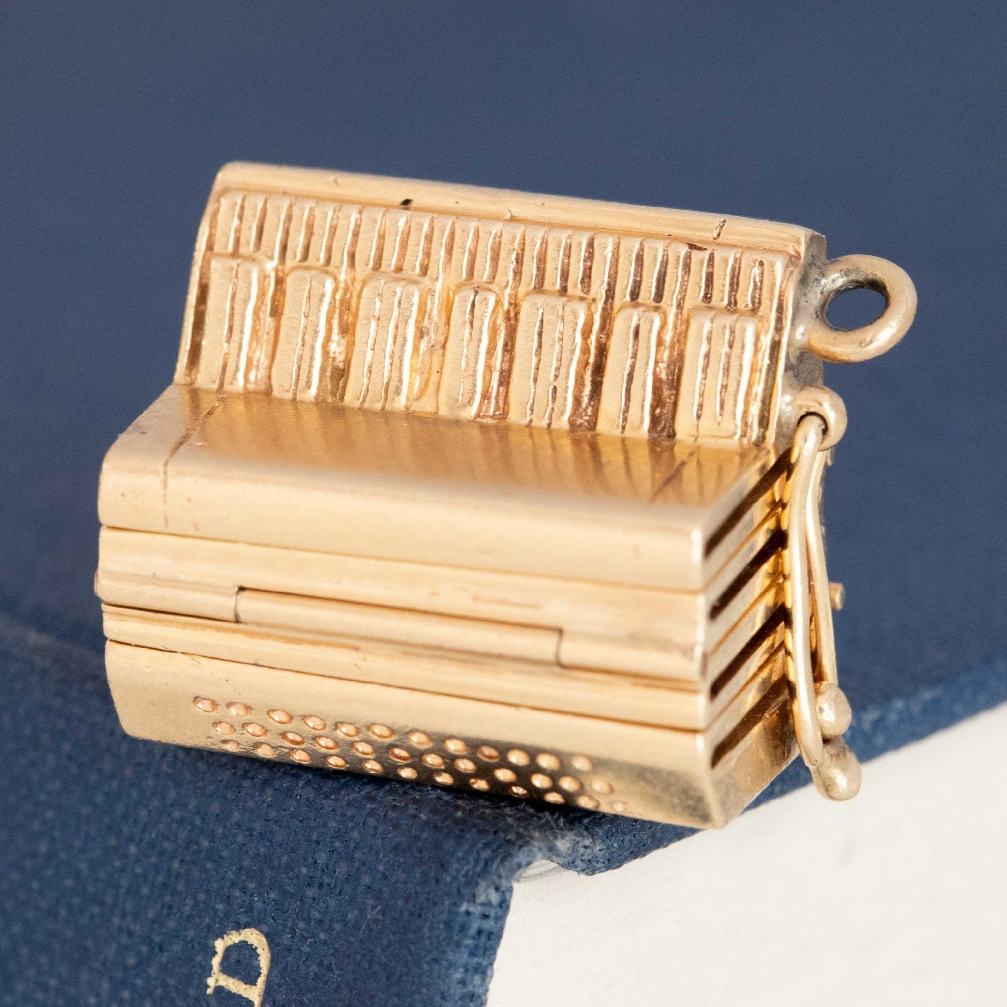 Close-up of vintage accordion charm locket in 14kt yellow gold, shown open with hinged pages.