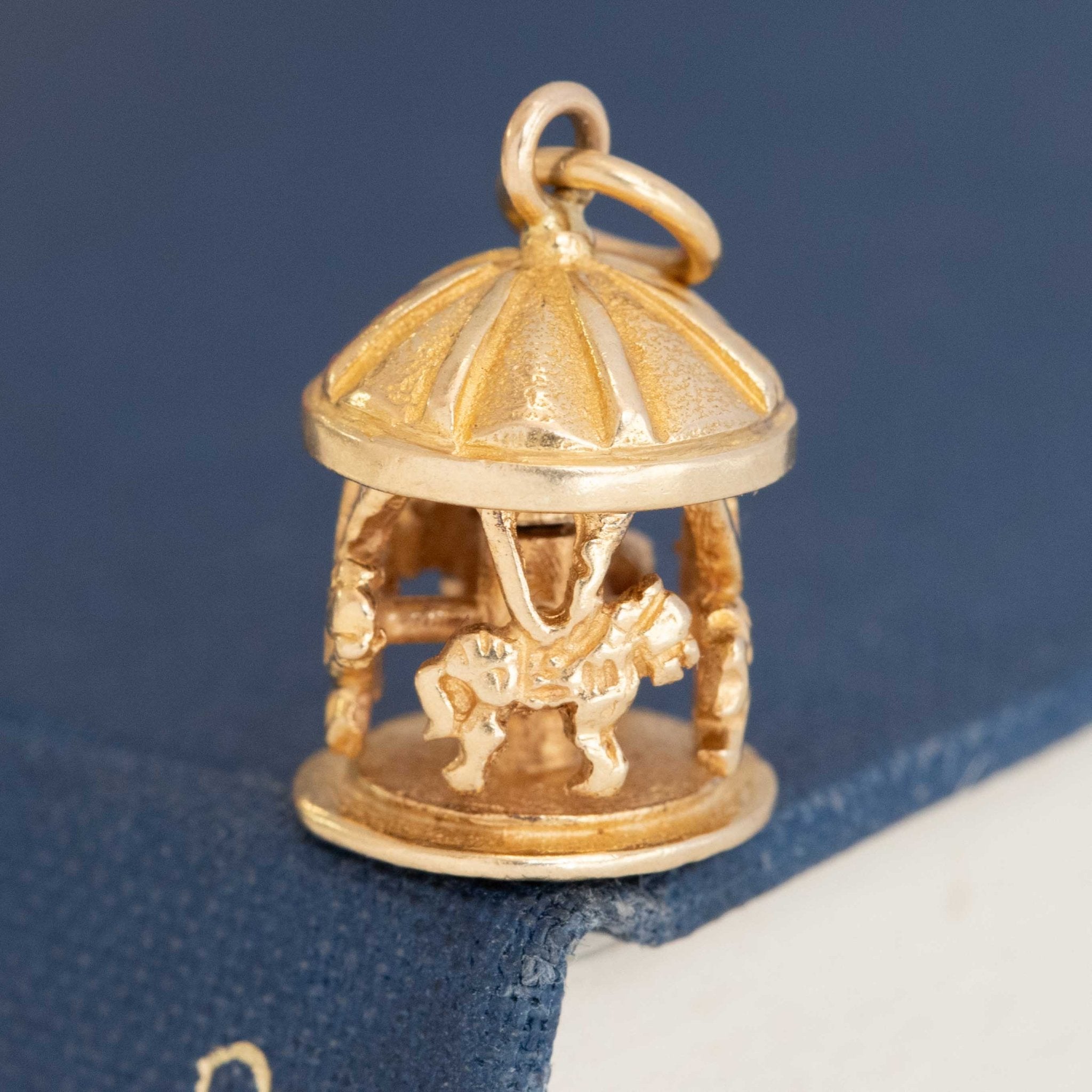 Close-up of vintage gold carousel charm with miniature horses under domed canopy.