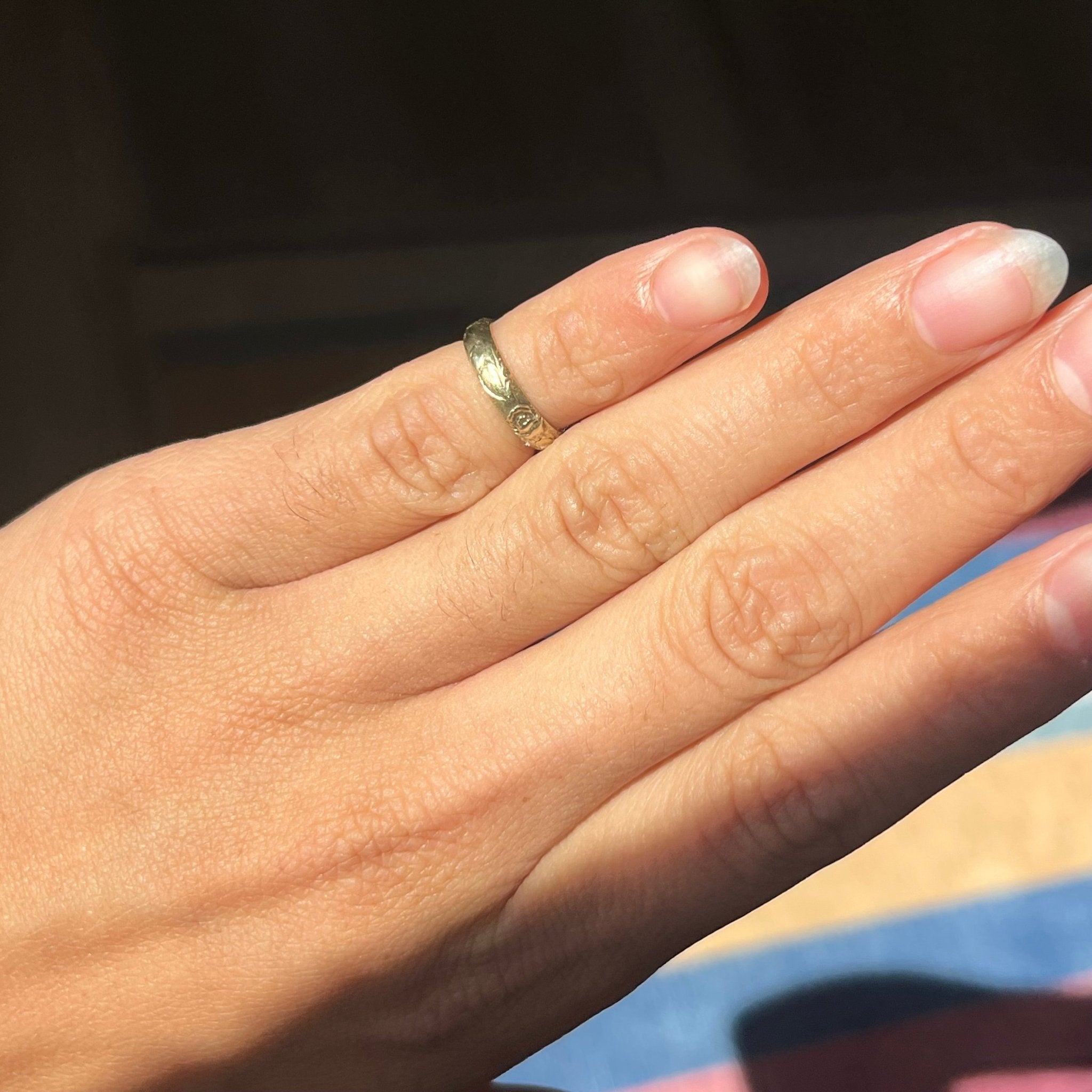 Hand shot of warm vintage yellow gold band with etched finish on pinky finger.