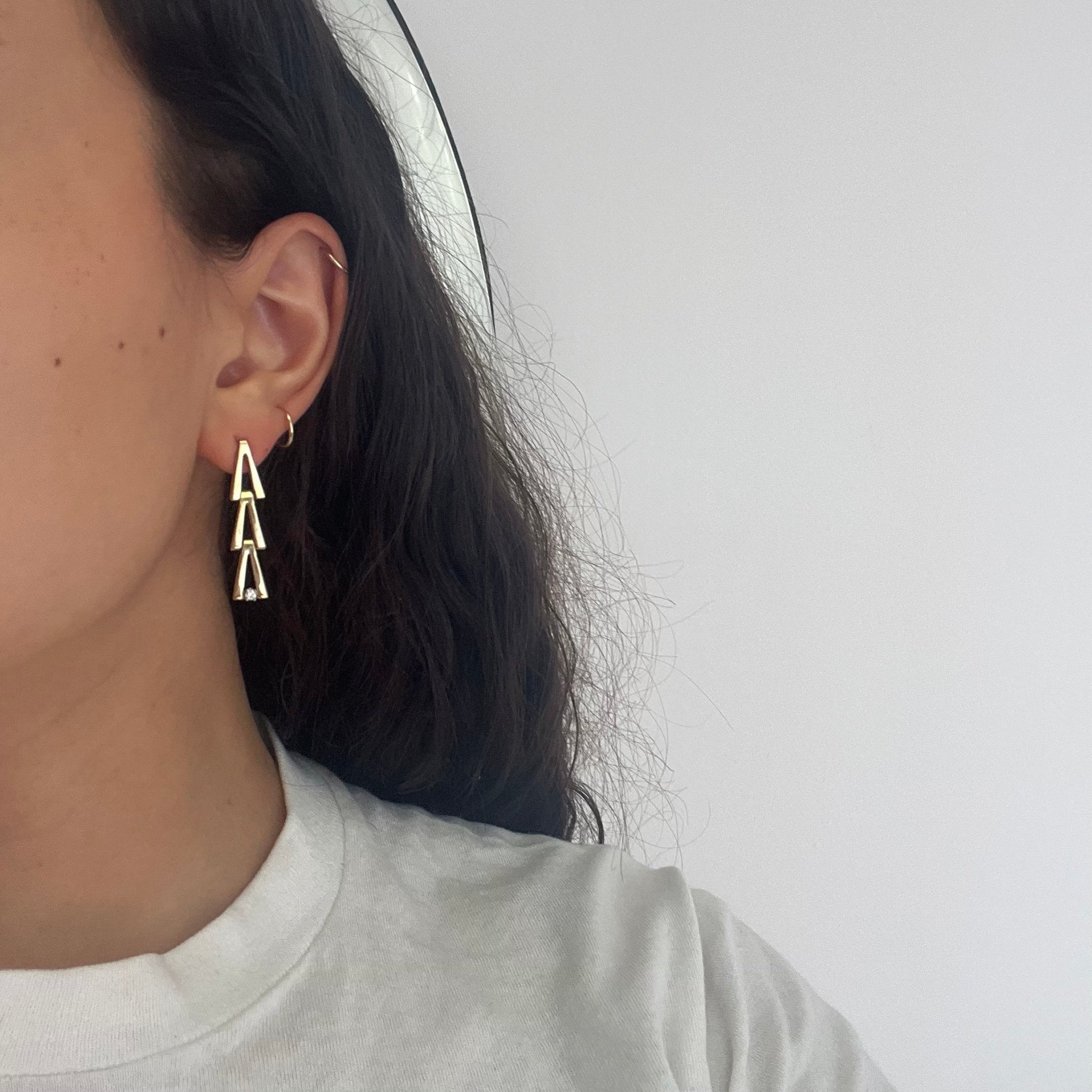 Close-up of geometric diamond drop earrings in yellow gold, showing linked V design.
