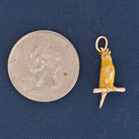 14k gold vintage charm depicting a canary on branch, enamel detailing visible shown next to a quarter for size reference