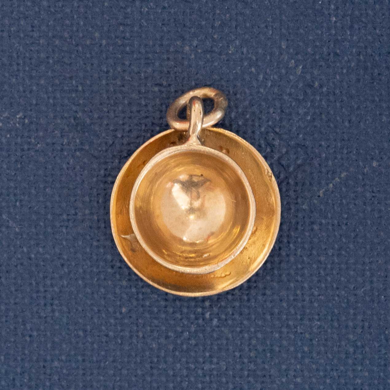 Close-up of miniature tea cup and saucer charm crafted in gold.