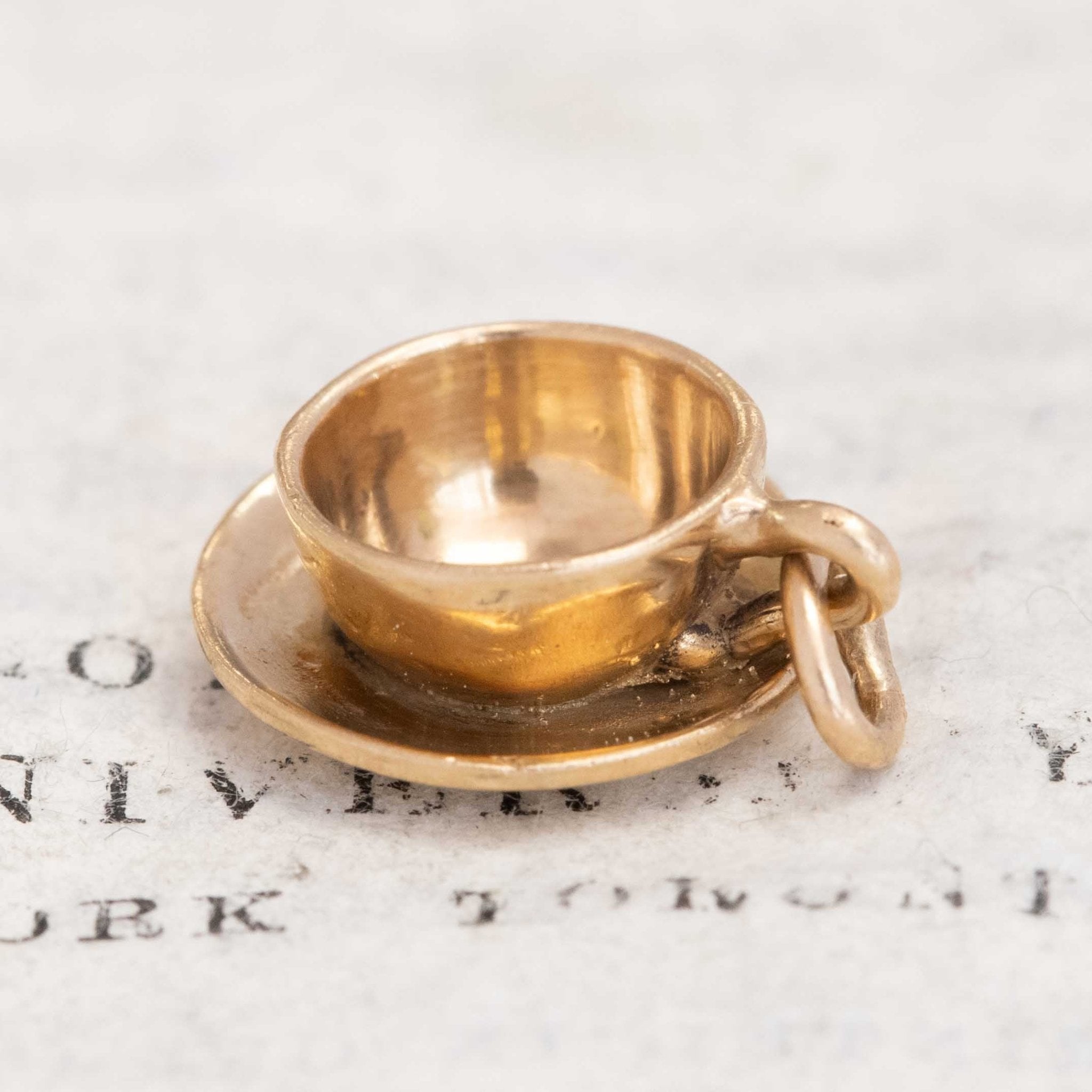 Vintage gold charm shaped like a cup and saucer, figural jewelry design.