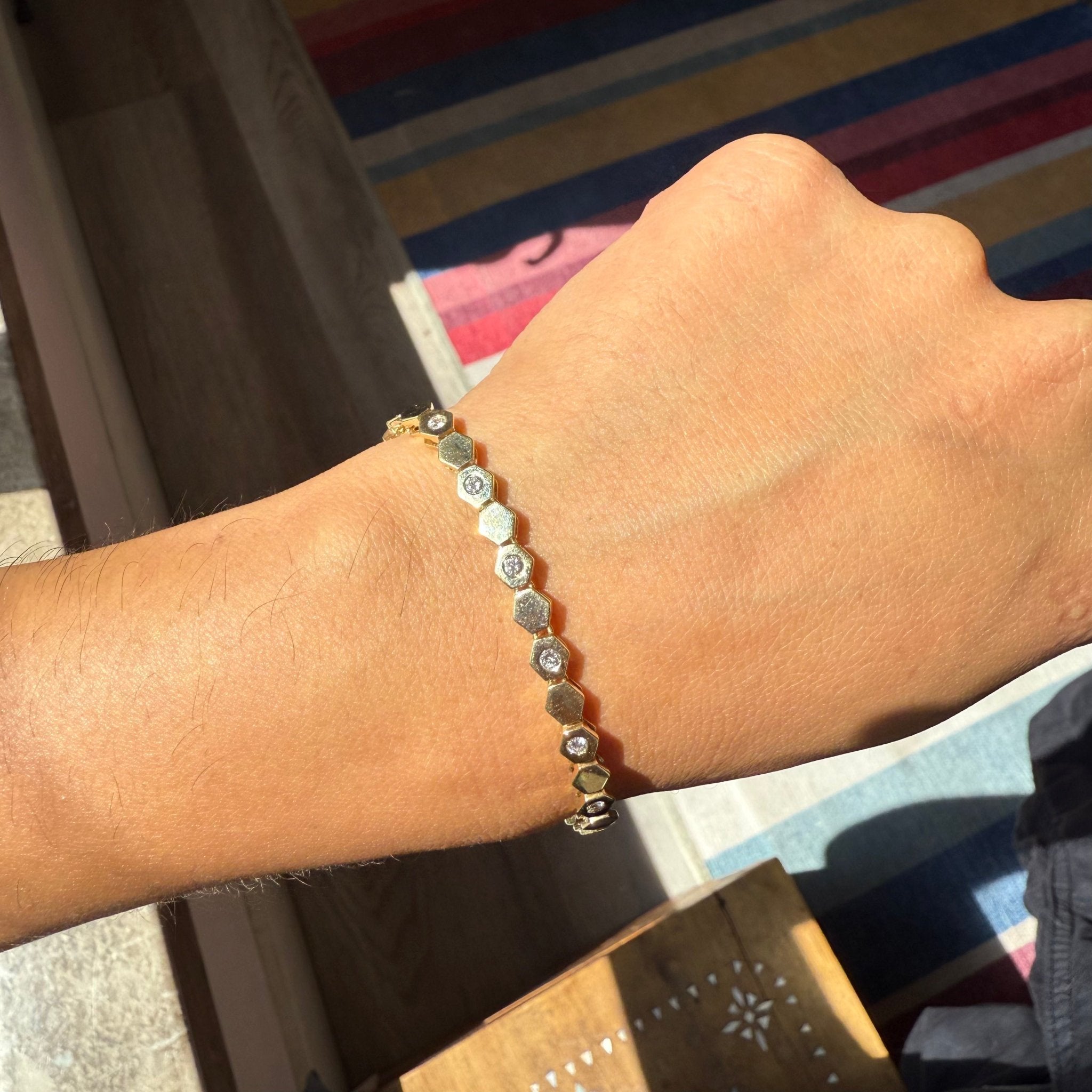 Close-up of gold bracelet featuring hexagonal links and scattered round diamonds on a wrist.