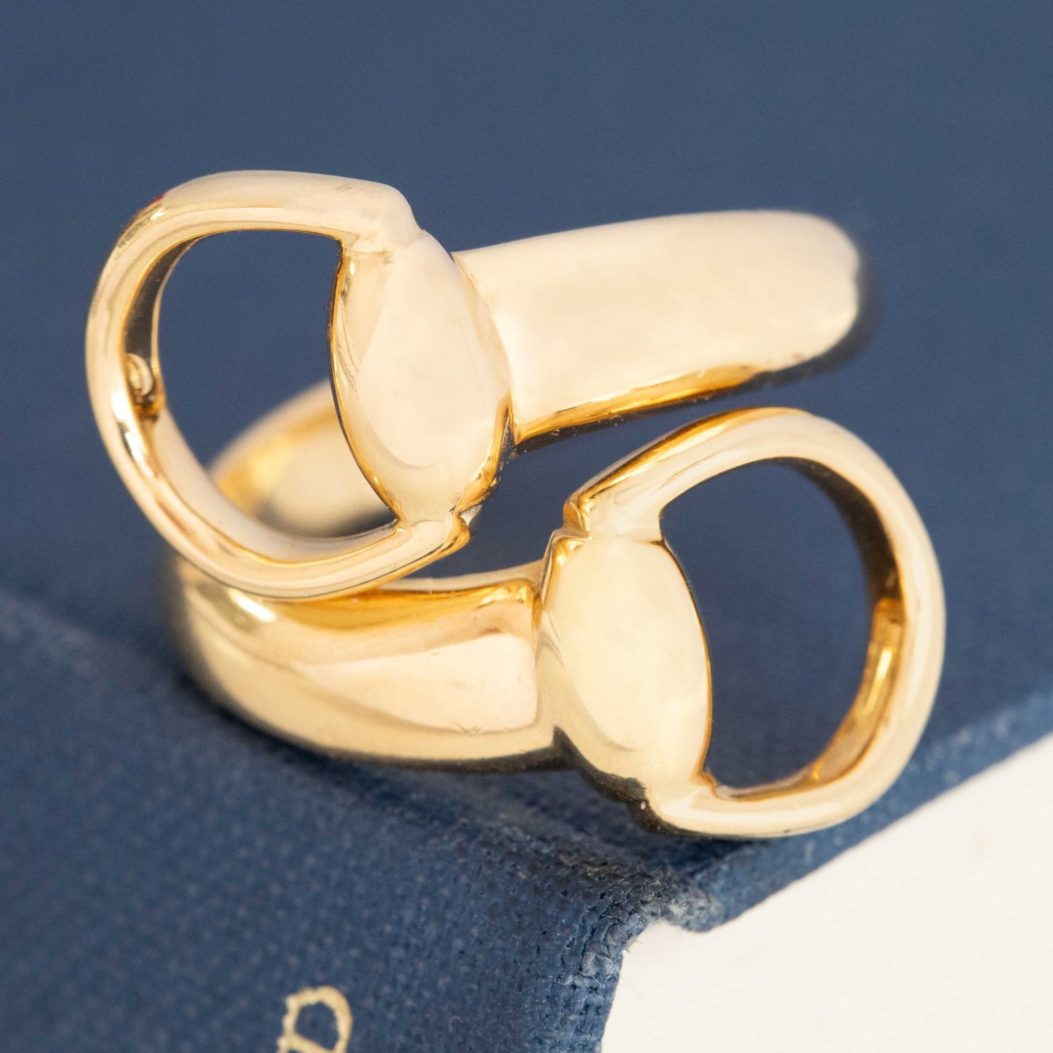 Close-up of Gucci gold bypass ring with bold horsebit motif, vintage style.