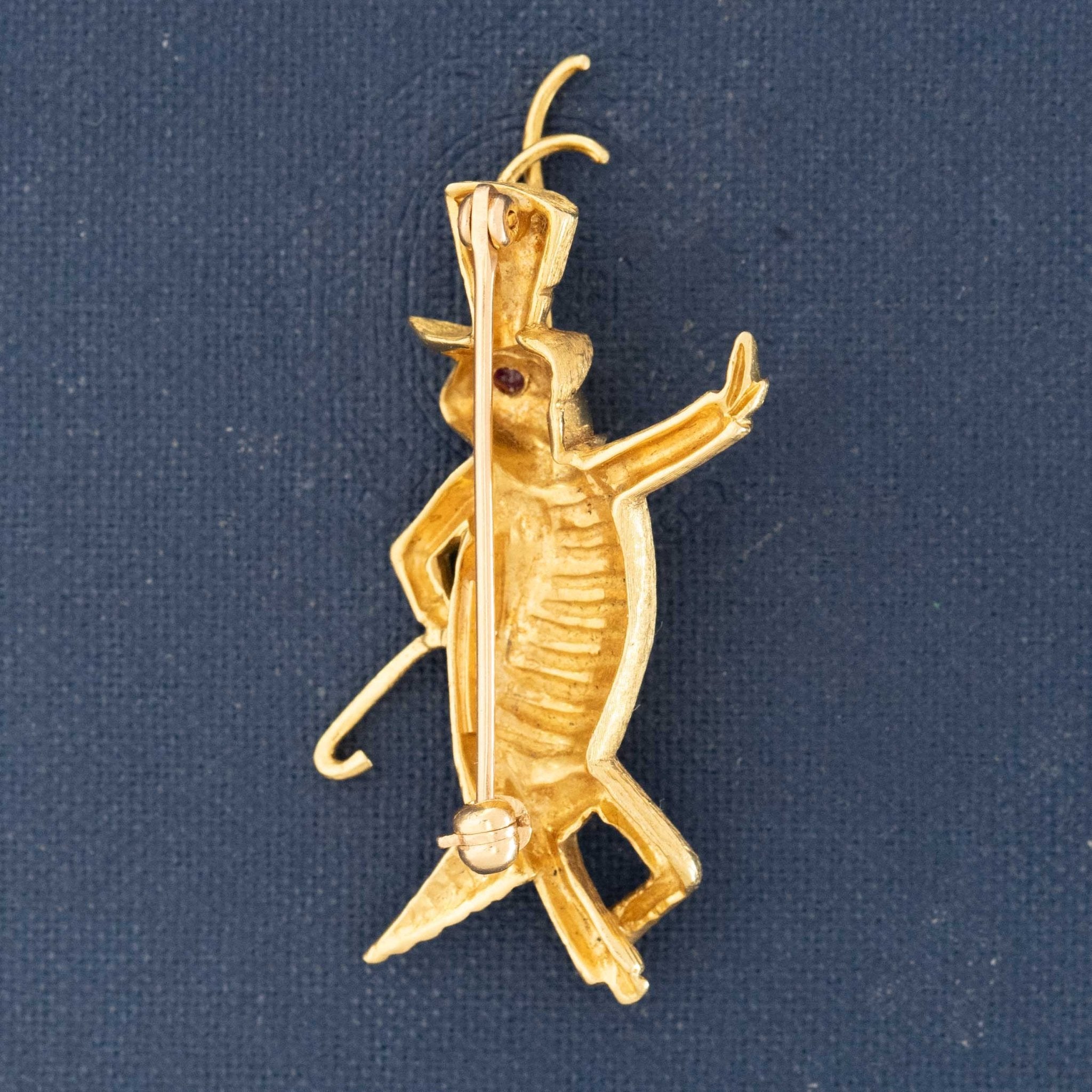 Collectible Disney-inspired gold brooch on navy background. Mid-century character brooch of Jiminy Cricket in top hat
