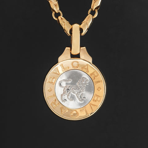 Vintage Bvlgari Leo zodiac pendant crafted in Italy from 18‑karat yellow gold with a contrasting stainless‑steel or white‑gold outer ring. The circular disc is engraved with the BVLGARI logo and features the Libra scales motif at the centre, and it bears hallmarks such as ‘Made in Italy’ and ‘750’.  Measuring roughly 1.23 inches in diameter and weighing about 13 grams, the pendant is numbered on the reverse and hangs from a substantial bail for easy wear as a charm or necklace.  