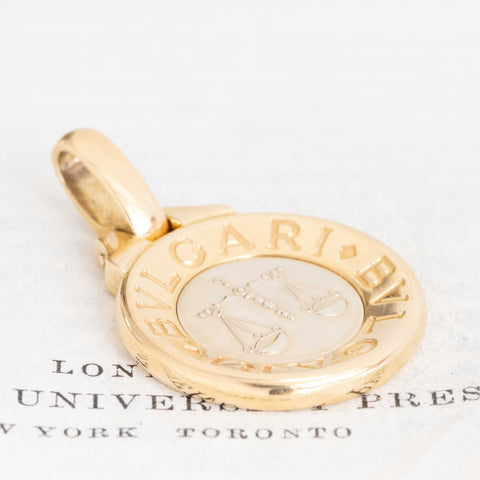 Vintage Bvlgari Libra zodiac pendant crafted in Italy from 18‑karat yellow gold with a contrasting stainless‑steel or white‑gold outer ring. The circular disc is engraved with the BVLGARI logo and features the Libra scales motif at the centre, and it bears hallmarks such as ‘Made in Italy’ and ‘750’.  Measuring roughly 1.23 inches in diameter and weighing about 13 grams, the pendant is numbered on the reverse and hangs from a substantial bail for easy wear as a charm or necklace.  