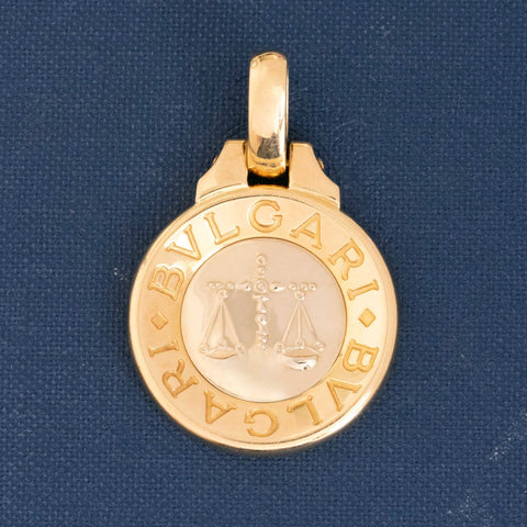 Vintage Bvlgari Libra zodiac pendant crafted in Italy from 18‑karat yellow gold with a contrasting stainless‑steel or white‑gold outer ring. The circular disc is engraved with the BVLGARI logo and features the Libra scales motif at the centre, and it bears hallmarks such as ‘Made in Italy’ and ‘750’.  Measuring roughly 1.23 inches in diameter and weighing about 13 grams, the pendant is numbered on the reverse and hangs from a substantial bail for easy wear as a charm or necklace.  