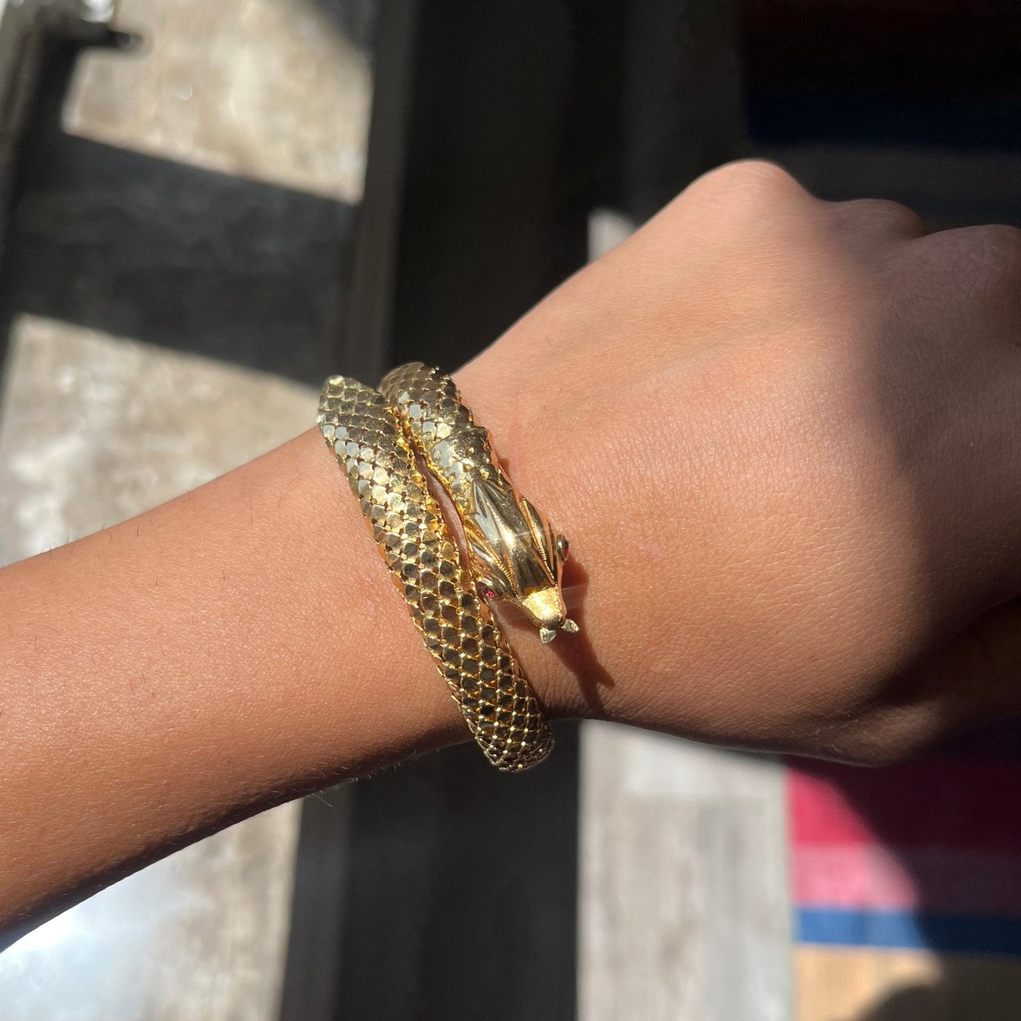 a beautiful vintage serpent themed bracelet with beautiful, realistic texture in rich yellow gold and ruby eyes being shown on a wrist