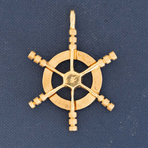 Close-up of yellow gold ship wheel pendant with six spokes, vintage nautical design.
